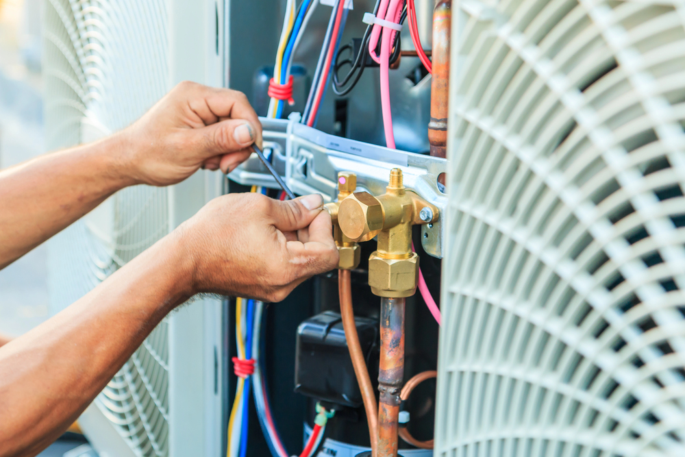 A person uses a tool to adjust wires and components inside an air conditioning unit.