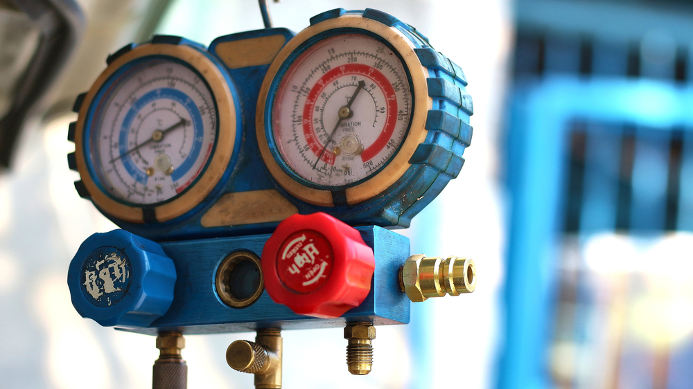 Close-up of a blue HVAC manifold gauge with two dials and red and blue control knobs, used for measuring pressure in refrigeration or air conditioning systems.