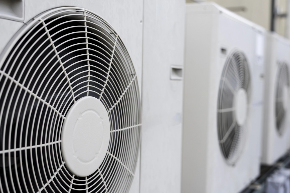 Close-up view of the front grills and fans of several outdoor air conditioning units lined up in a row.