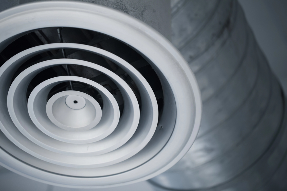 Close-up view of a circular air vent attached to a metal duct on a ceiling.