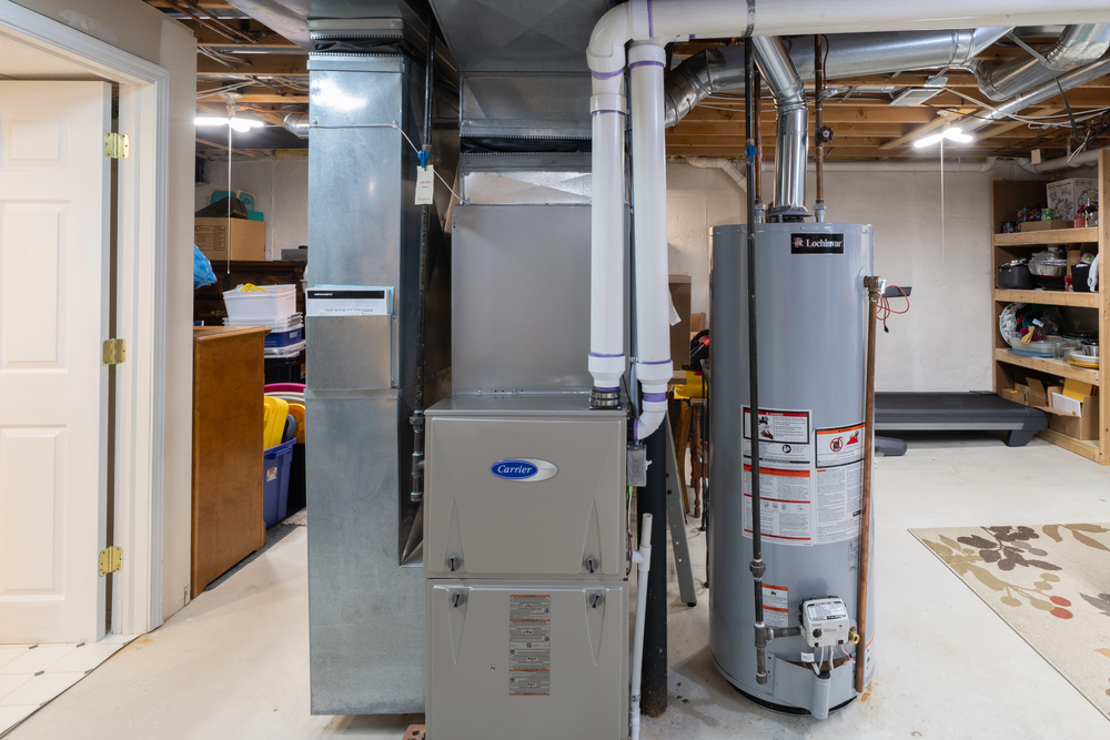 Furnace and water heater installed in a basement utility area with exposed pipes and organized storage shelves in the background.