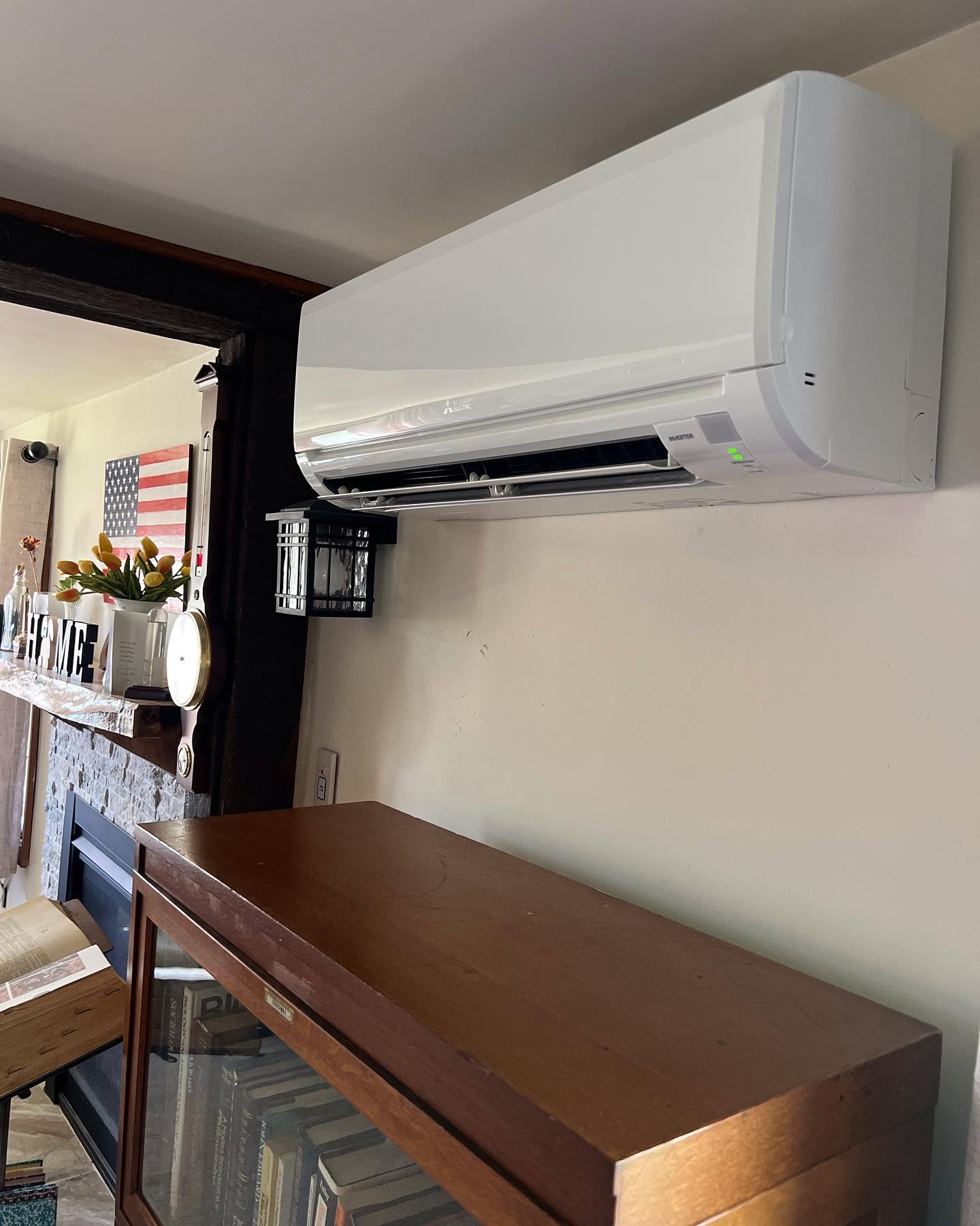 A wall-mounted air conditioning unit is installed above a bookshelf in a living room with a fireplace and American flag decor.